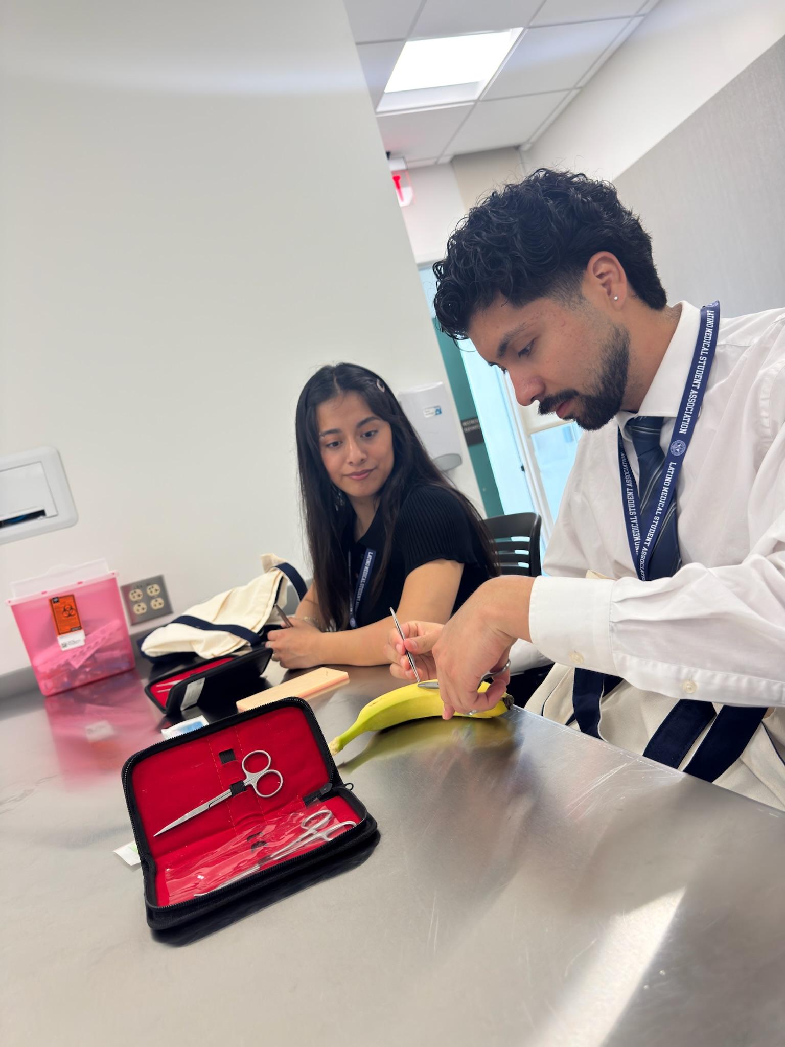 Two students in LMSA lanyards practicing suturing on a banana.